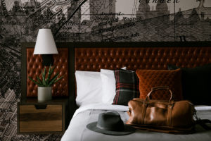 Guestroom at Bobby Hotel in Nashville TN featuring bed with custom wallpaper and leather bag and hat sitting on bed